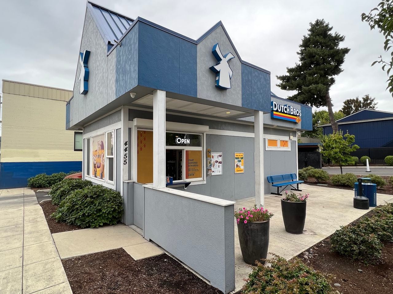 A blue-and-gray Dutch Bros drive-thru stand, with the company’s windmill logo on the roofline.