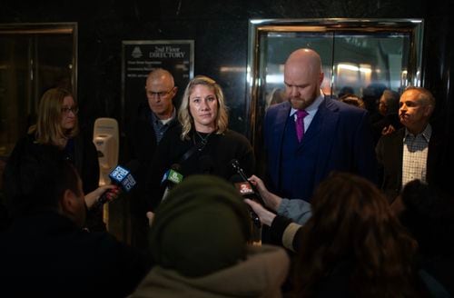 A woman and a man in a suit stand in front of a gaggle of reporters